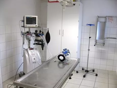 Behandlungsraum mit medizinischem Monitor, Beatmungsgerät, Edelstahluntersuchungstisch und Infusionsständer auf Rollen