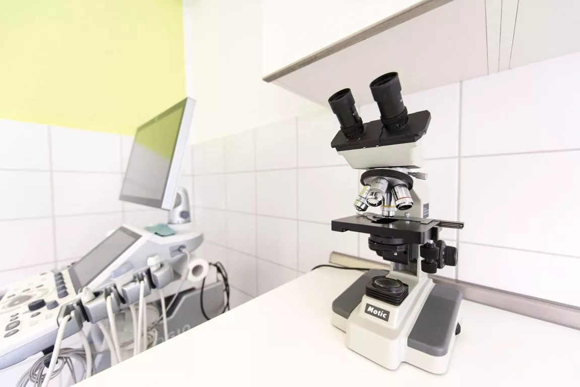 Mikroskop auf einem weißen Labortisch vor medizinischem Ultraschallgerät in heller Praxis