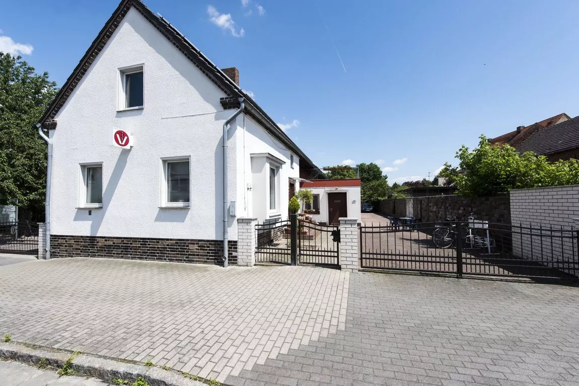 Einfamilienhaus mit weißer Fassade und dunklem Satteldach an einer ruhigen Straße mit Gehweg und Gartenzaun