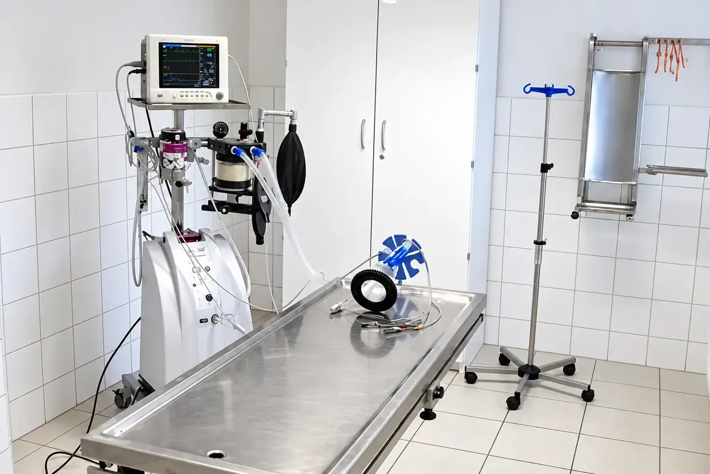 Behandlungsraum mit medizinischem Monitor, Beatmungsgerät, Edelstahluntersuchungstisch und Infusionsständer auf Rollen